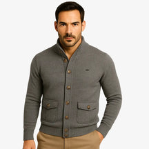 Modelo masculino usando cardigan cinza escuro de botão com bolsos frontais, estilo social casual, calça chino bege. Ideal para outono/inverno