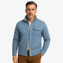 Homem vestindo jaqueta masculina azul com gola alta, bolso superior e fechamento por botões